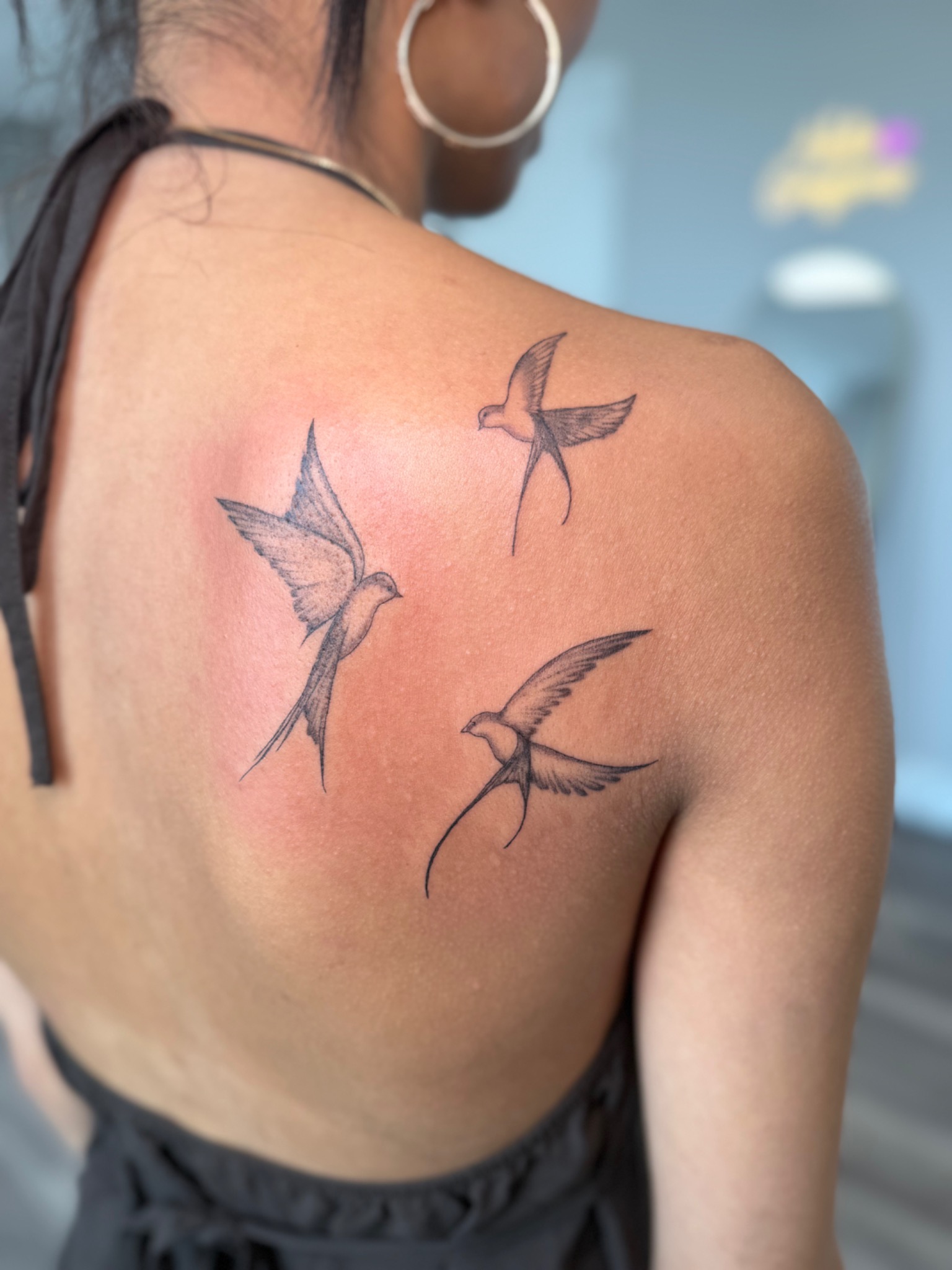 Three delicately shaded bird tattoos across a client’s shoulder blade, by Abigaille Palileo